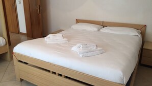 Un lit bien fait, avec du linge de lit et des serviettes blanches, une tête de lit en bois et une armoire en bois équipée d’un téléphone et d’un interrupteur.