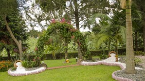 A garden with a central archway, surrounded by a well-maintained lawn and various plants. - Sheevy's Bed N Breakfast (Fort Portal)