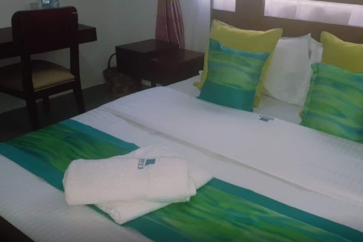 A hotel room with a bed, a chair, a nightstand, and a window with curtains.
