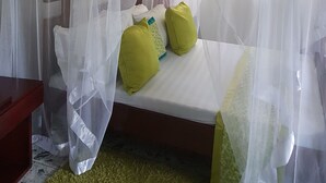 A bedroom with a canopy bed, a bedside table, and a green rug. - Sheevy's Bed N Breakfast (Fort Portal)