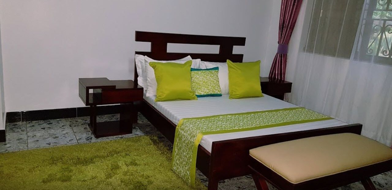 Une chambre à coucher avec un lit, une table de chevet, une commode, un tapis vert et une fenêtre avec des rideaux.