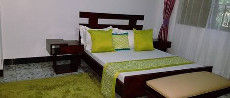 Une chambre à coucher avec un lit, une table de chevet, une commode, un tapis vert et une fenêtre avec des rideaux.