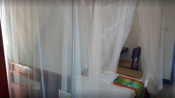 A room with a bed covered by a white canopy, a small table, and a chair.