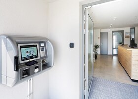 Um quiosque de check-in automático e uma área de recepção com balcão de madeira.