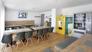 Un comedor moderno con mesas de madera y sillas negras, una máquina expendedora y un refrigerador.
