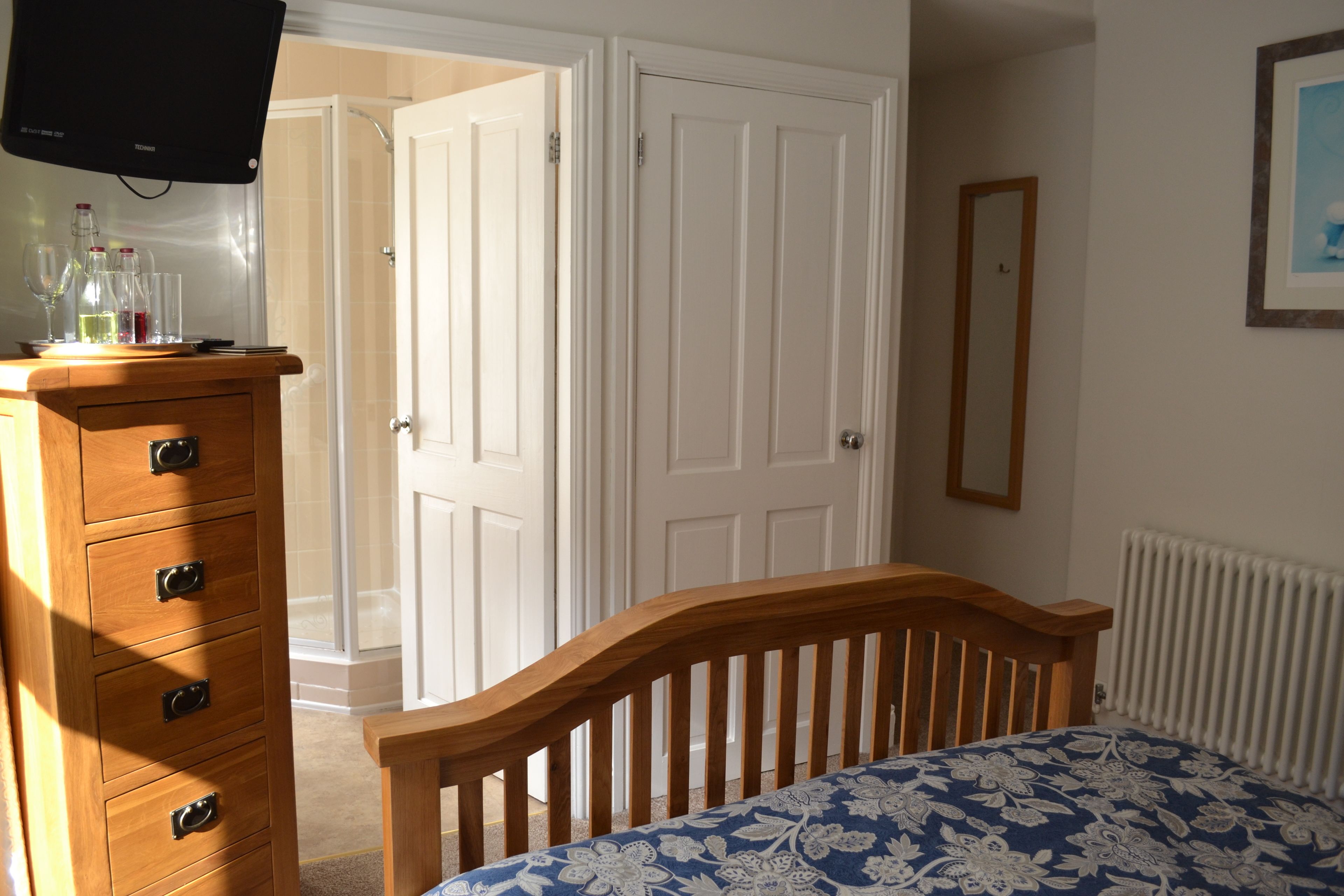 Een slaapkamer met een houten dressoir, een bed met een bloemenbedekking, een televisie bovenop het dressoir en een witte deur die naar een andere kamer leidt.