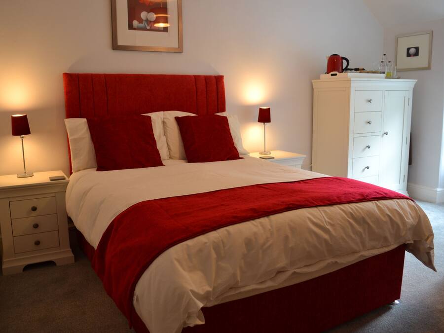 A neatly made bed with red and white bedding, two bedside tables with lamps, a white dresser, and a framed picture on the wall.