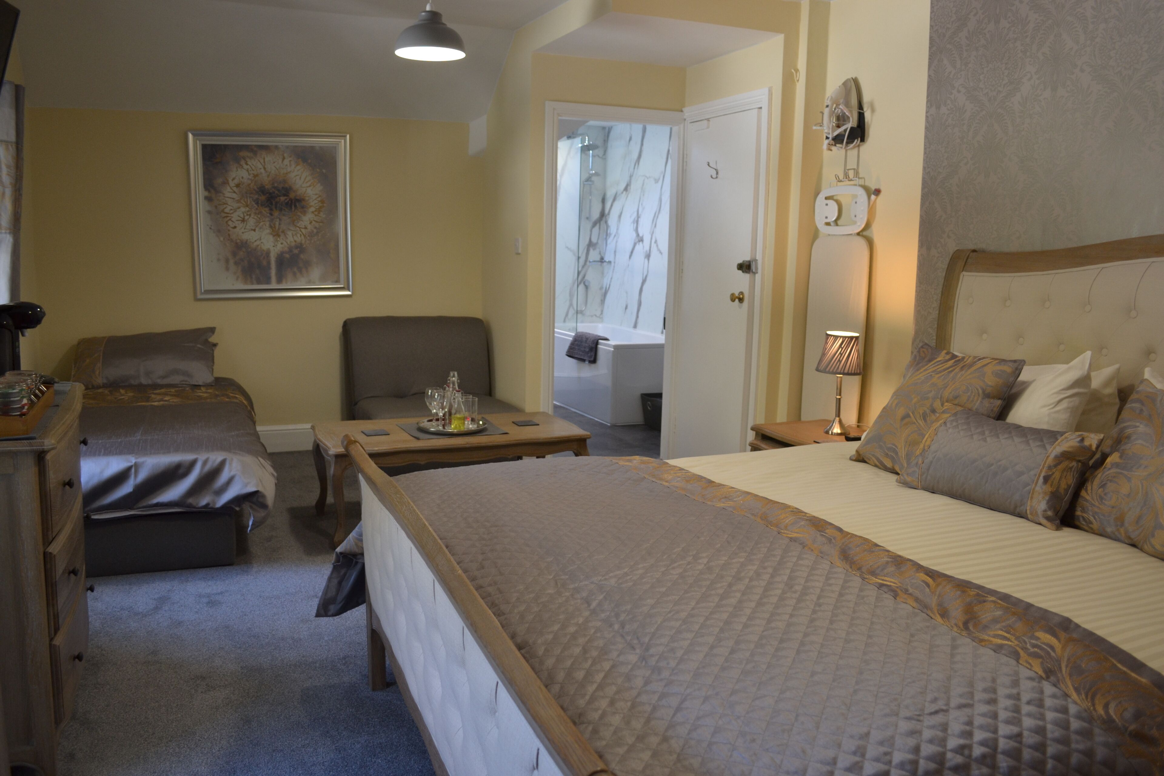 A hotel room with two single beds, a sitting area with a table and chairs, a bedside lamp, and a large window.