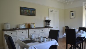 Zona de dinar amb taula blanca preparada per a quatre, una cafetera i un quadre a la paret.