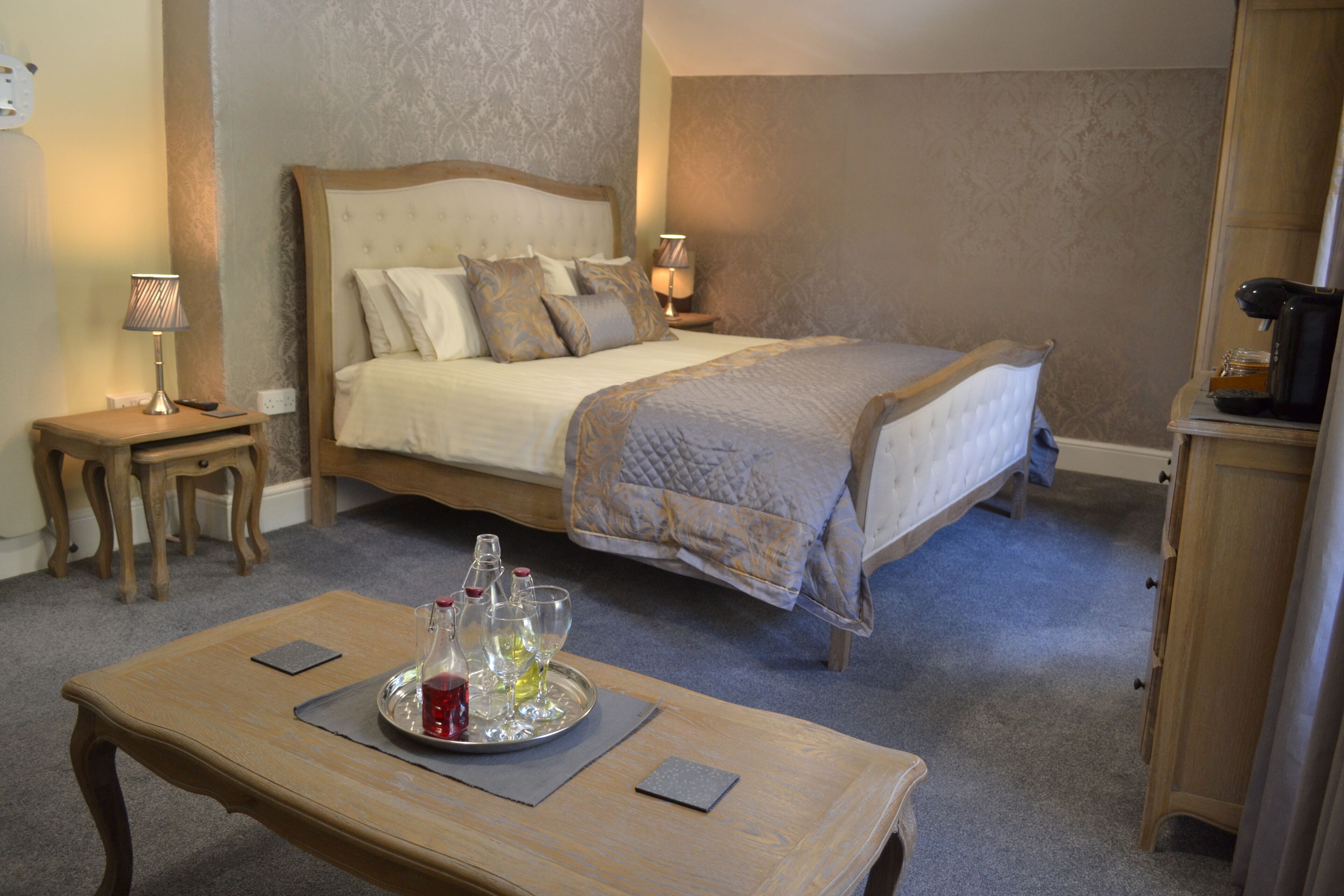 A bedroom with a bed, bedside tables, a coffee machine, and a tray with bottles and glasses.