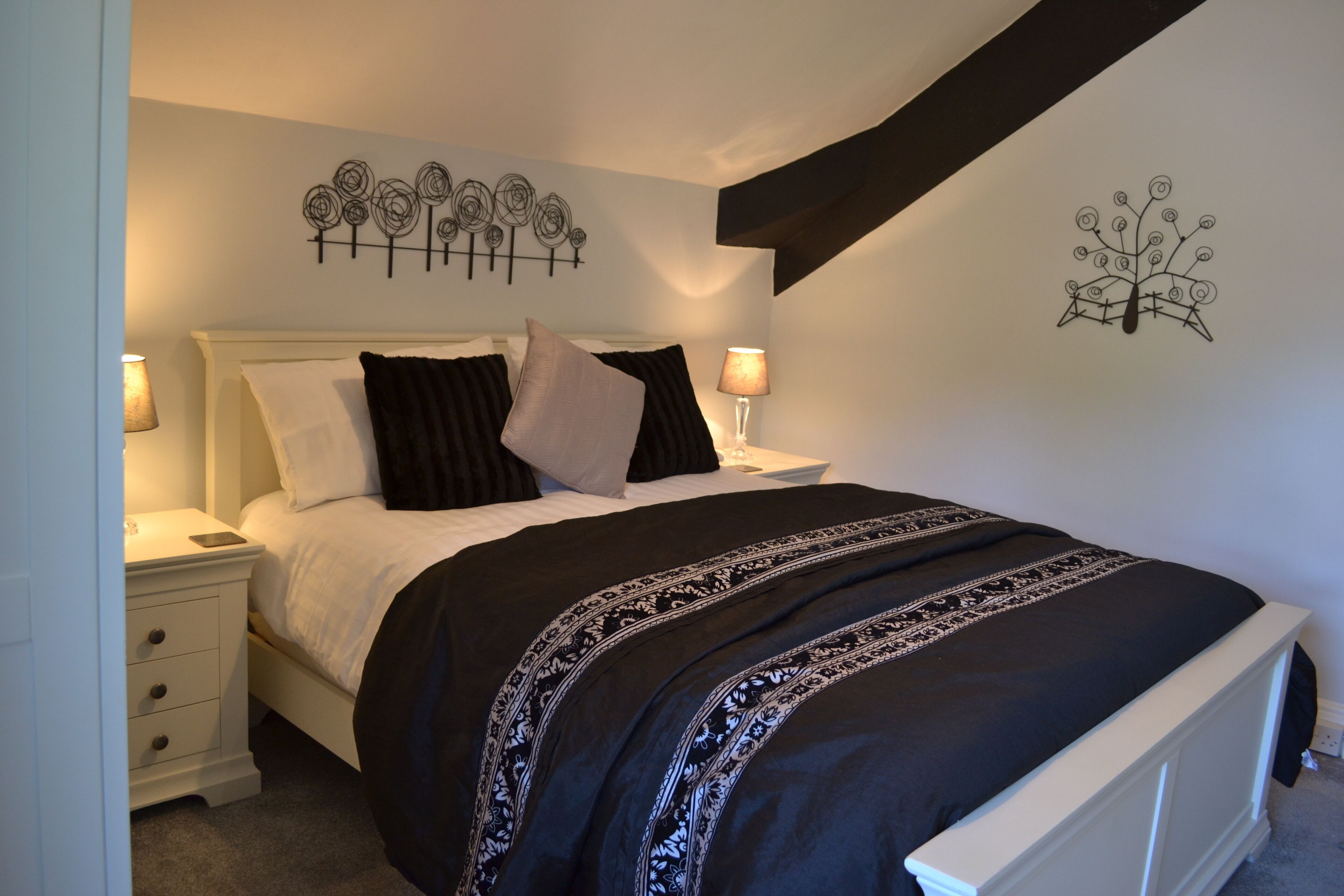A neatly made bed with a black and white patterned bedspread, a white headboard, and two bedside lamps.