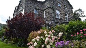 Edifici de pedra amb nombroses finestres i un jardí ple de flors diverses.