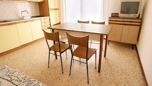 A compact kitchen with a dining table and chairs, a television, and a window with curtains. - Euroresidence n.4 (Jesolo)