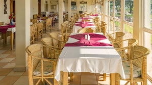 A dining area with wicker chairs and tables, large windows, and ceiling fans. - Sunrise Apartments Hotel (Fort Portal)