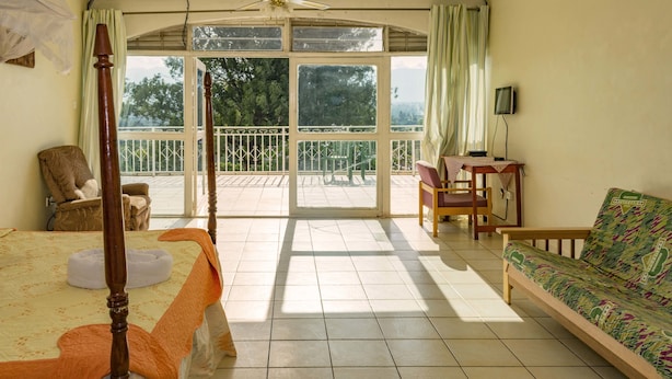 A room with a bed, a sofa, a chair, a table, and a balcony with a railing. - Sunrise Apartments Hotel (Fort Portal)