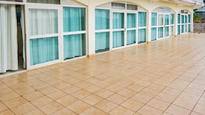A long corridor with large windows and doors, tiled floor, and a railing along the right side. - Sunrise Apartments Hotel (Fort Portal)