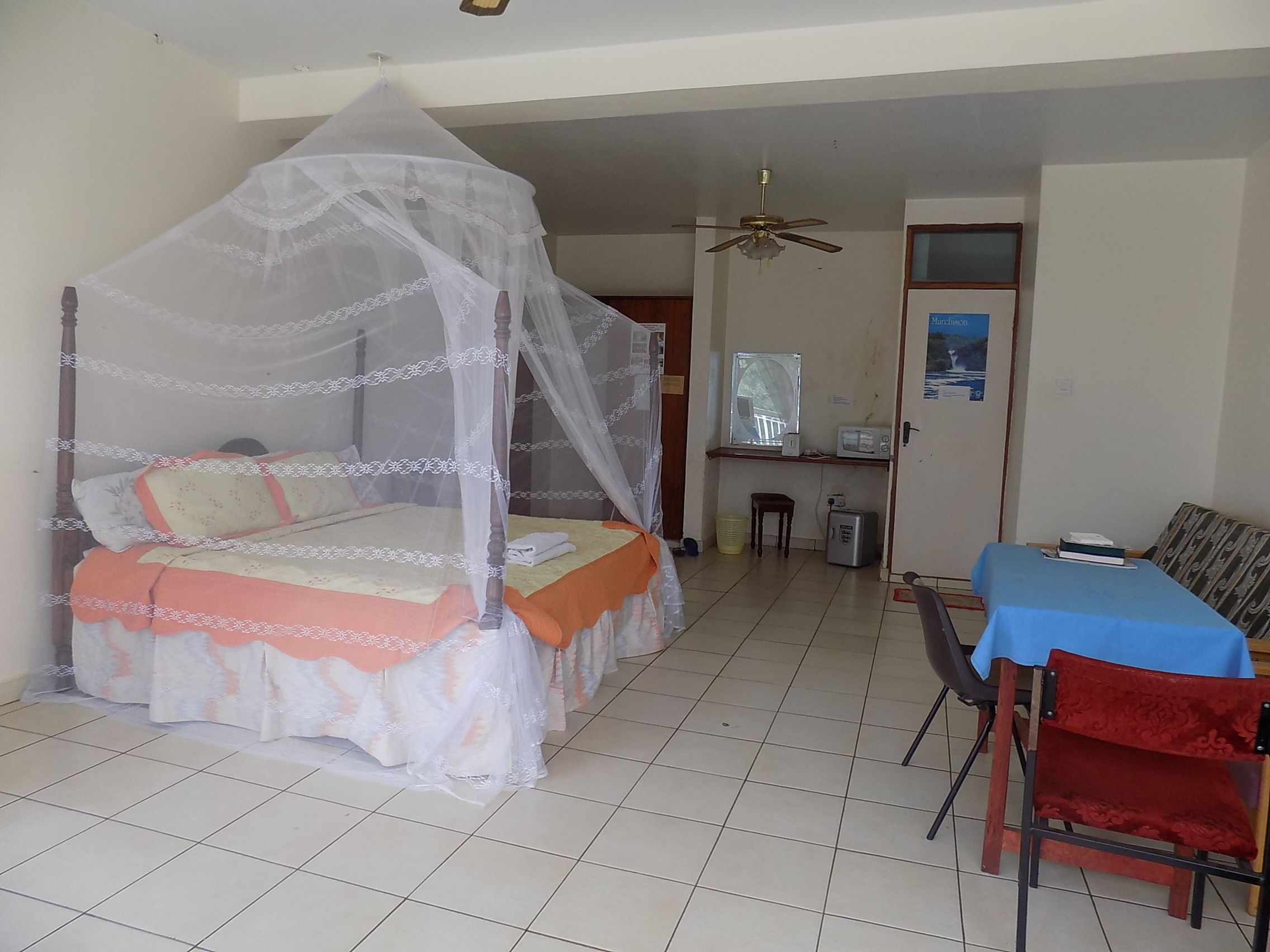 A room with a bed under a mosquito net, a desk with a chair, and a small table with a chair.