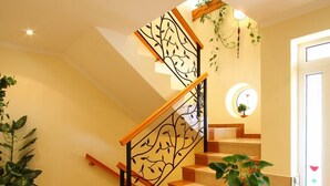 Una escalera con barandilla de madera y pasamanos negro, que lleva a una plataforma con una planta en maceta.