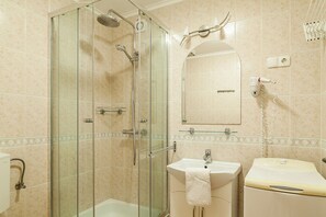 Baño con ducha envuelta en vidrio, lavamanos, espejo y secador de pelo en la pared.