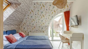 Un dormitorio con techo inclinado, cama con ropa de cama azul y roja, escritorio con silla y televisor en la pared.