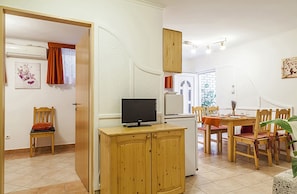 Un comedor con una mesa dispuesta para cuatro personas, un televisor sobre un mueble de madera y una silla con cojín.