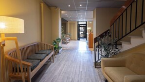 A hotel lobby with a wooden bench, a sofa, a staircase, and a reception desk. - L'Aptois Hotel (Apt)