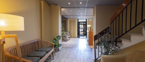 Un hall d’hôtel avec un banc en bois, un canapé, un escalier et un comptoir d’accueil.