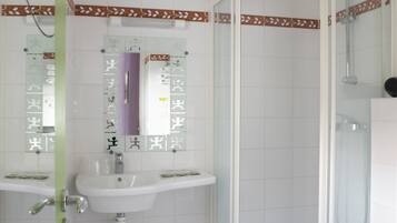 Un baño con ducha, dos lavamanos y un inodoro.