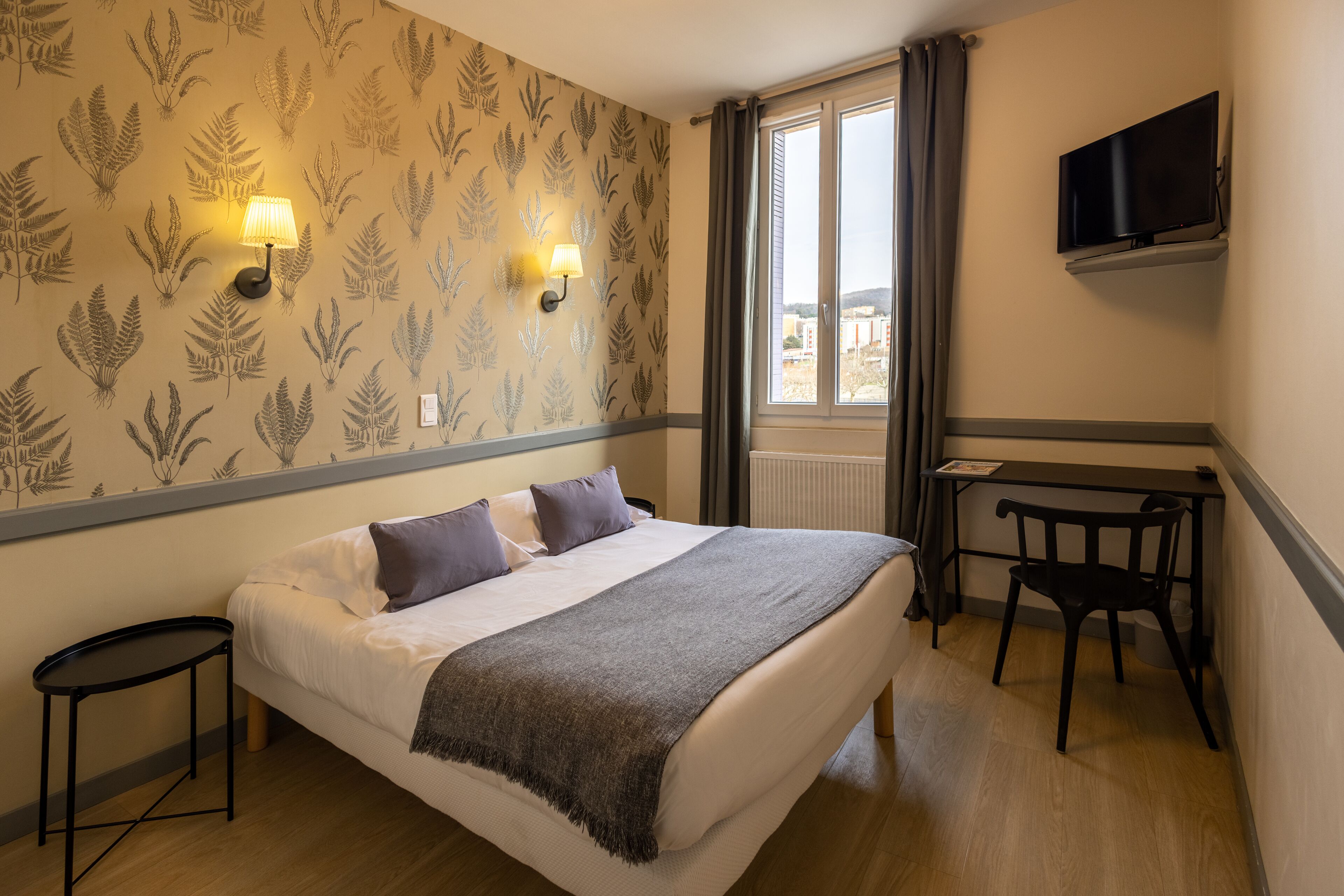 Habitació d'hotel amb llit, escriptori, cadira, televisió i finestra amb cortines.