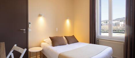 A bedroom with a bed, bedside lamps, a chair, a small table, and a window with a view.