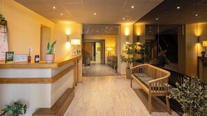 A hotel lobby with a reception desk, wooden bench, potted plants, and a staircase. - L'Aptois Hotel (Apt)