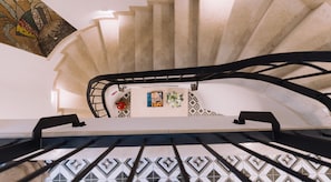A spiral staircase with a black handrail and patterned floor tiles.