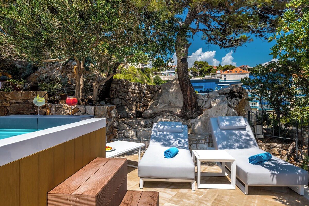 Un espace aménagé au bord de la piscine, avec des chaises longues, un banc en bois et un mur en pierre.