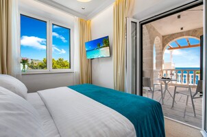 Quarto de hotel com cama, televisão na parede e varanda com vista para o mar.