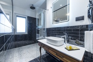 Un baño moderno con un lavabo blanco, baldosas de mármol oscuro y un espejo grande.