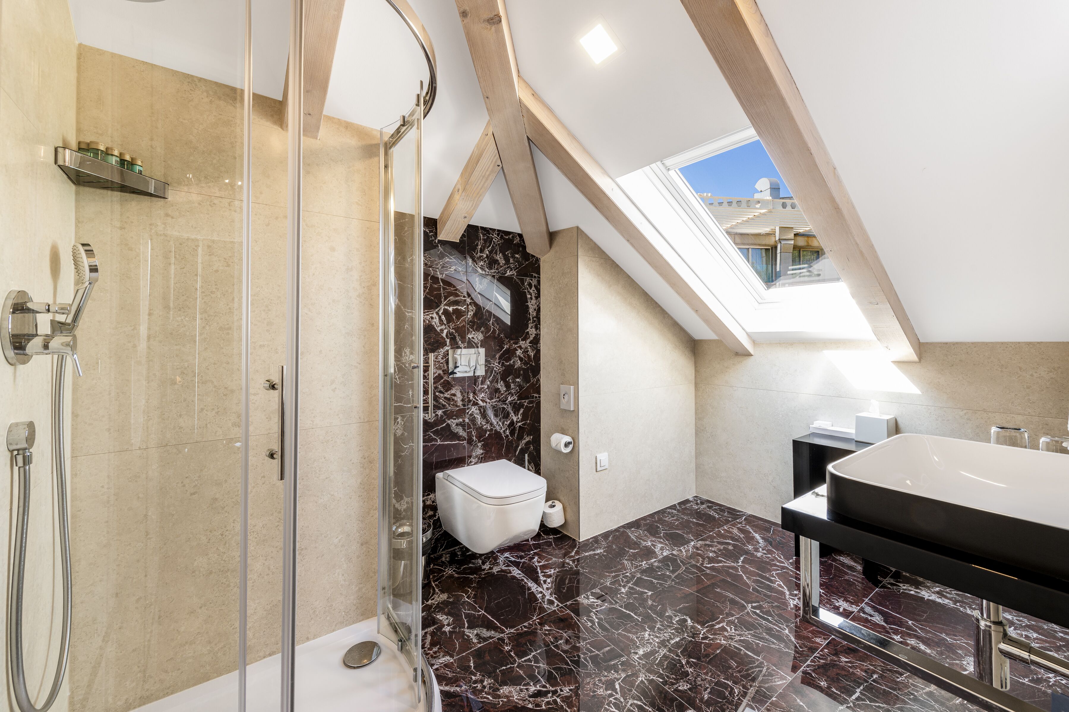 A modern bathroom with a glass-enclosed shower, a marble floor, and a skylight.