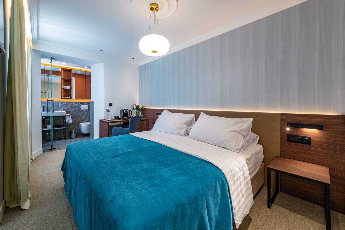 A hotel room with a bed, bedside table, and a desk with a chair.