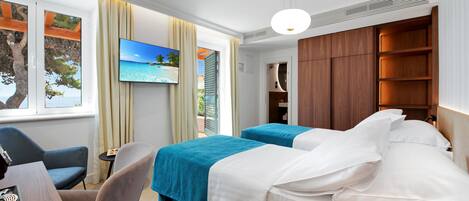 A hotel room with two beds, a desk, a chair, a TV, and a view of the sea.