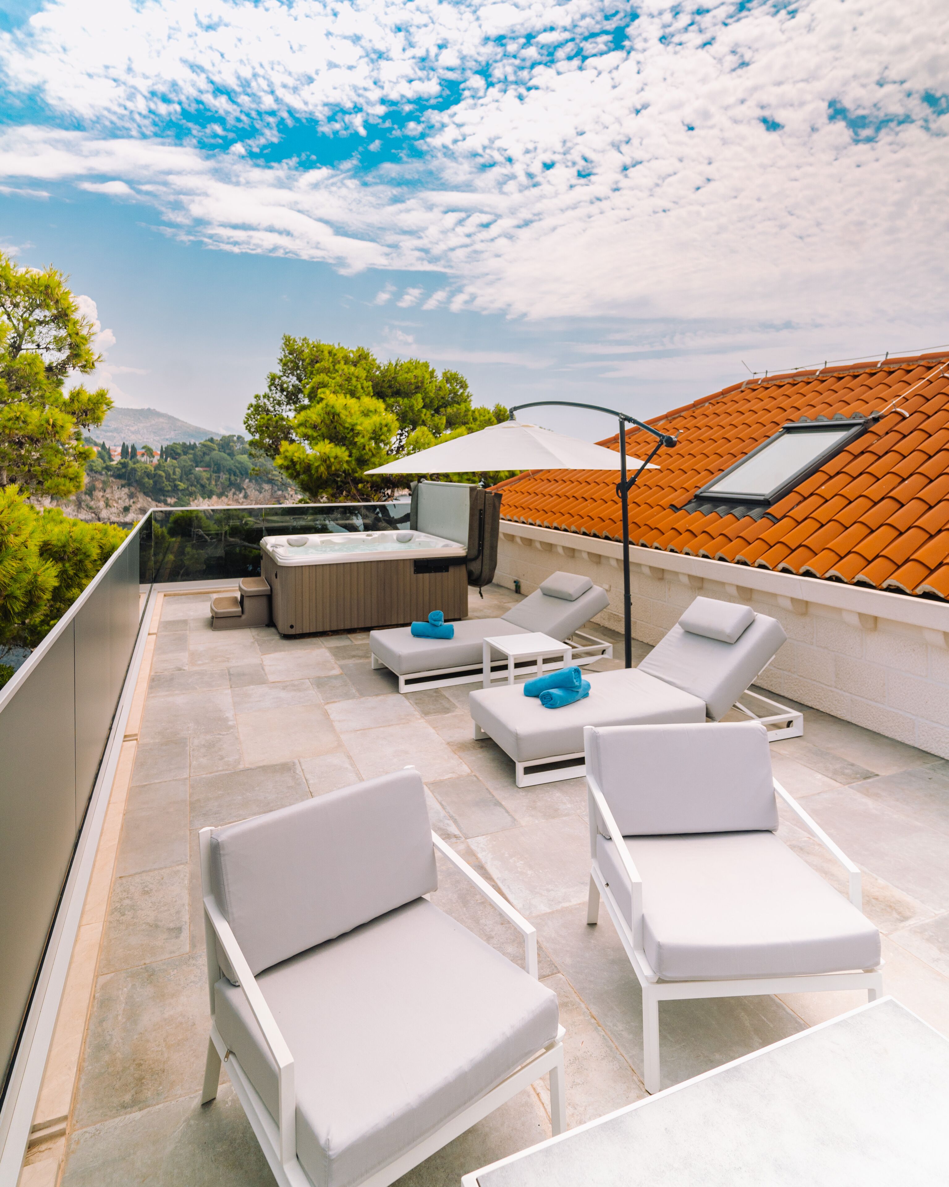 Une terrasse sur le toit avec des chaises longues blanches, un jacuzzi et une table avec des parasols.