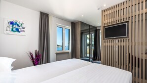Quarto de hotel moderno com uma cama grande, televisão de tela plana montada em um painel de madeira, janela com cortinas e um quadro na parede.