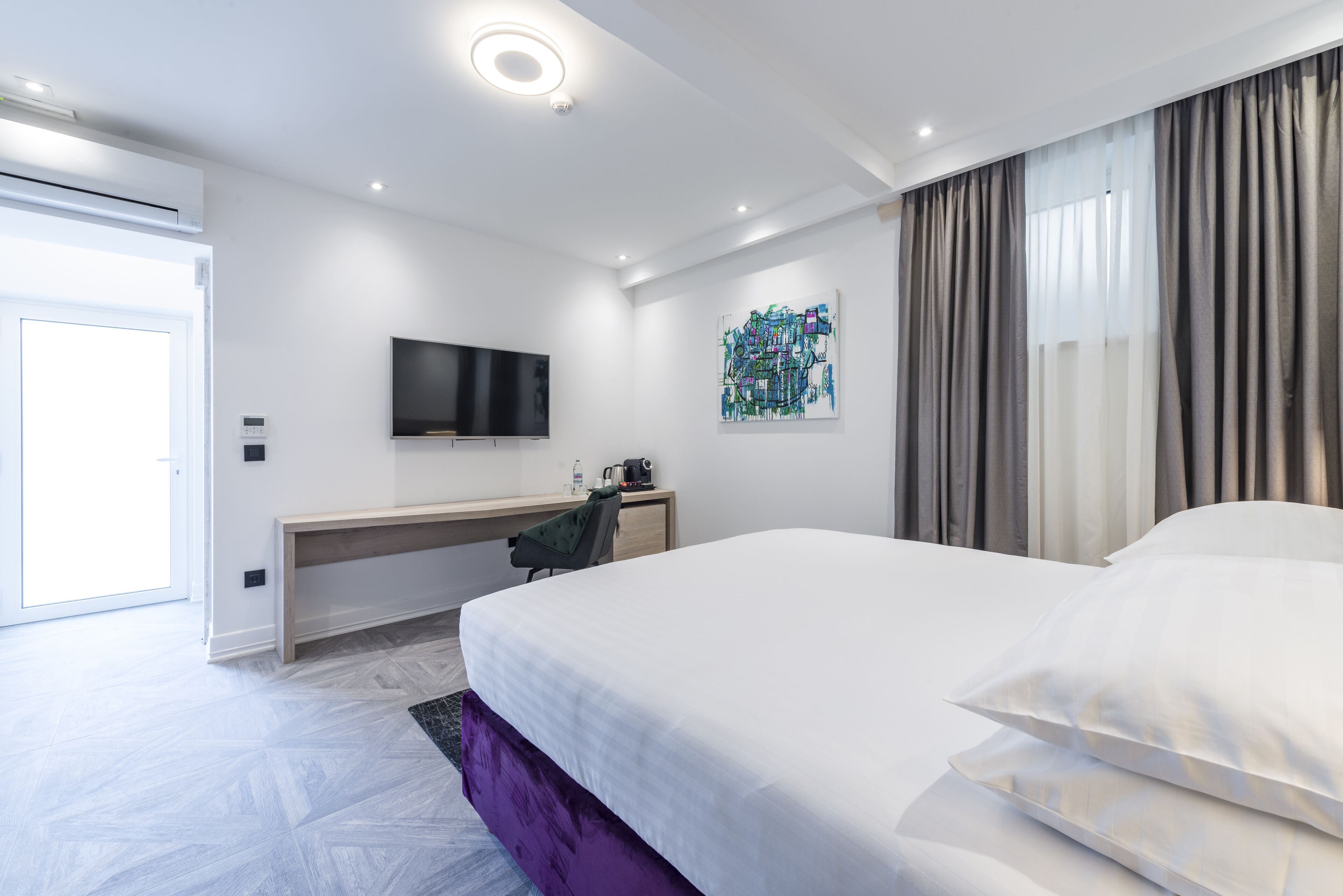 Une chambre d’hôtel moderne avec un grand lit, un bureau avec une chaise, un téléviseur à écran plat et un tableau au mur.