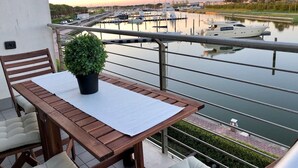 A balcony with a table, chairs, and a potted plant, overlooking a marina with boats and a calm body of water. - Libeccio (Jesolo)