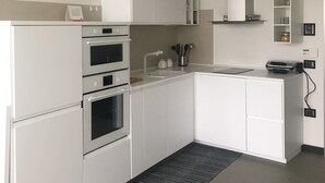 A modern kitchen with white cabinetry, a built-in oven, a sink, and a small countertop with a kettle and utensils. - Libeccio (Jesolo)