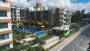 A multi-story hotel with a swimming pool, palm trees, and a clear sky. - Cobertura Luxor Paulo Miranda (João Pessoa)
