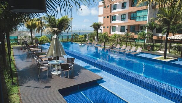 A hotel pool area with lounge chairs, umbrellas, and a view of the ocean. - Cobertura Luxor Paulo Miranda (João Pessoa)