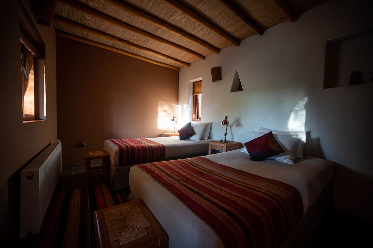 A room with two beds, wooden beams on the ceiling, a small table, and a window.