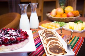A breakfast table with pancakes, a berry dessert, and a fruit bowl. - Naturalis (San Pedro de Atacama)