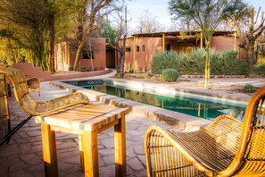 A pool area with wicker chairs and a stone patio. - Naturalis (San Pedro de Atacama)