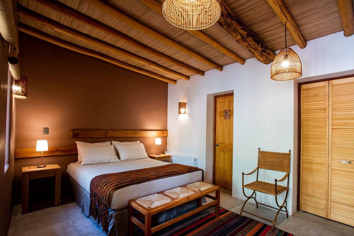 A cozy bedroom with a wooden bed, two bedside lamps, a woven chair, and a large wardrobe.