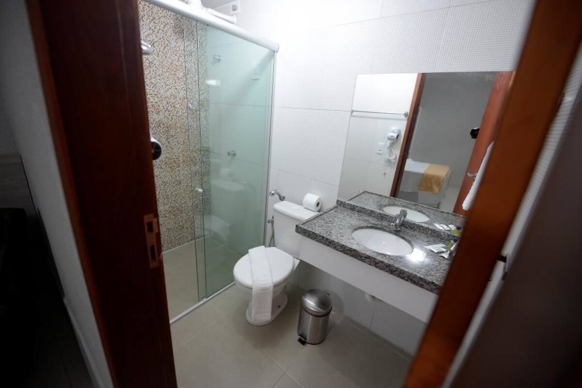 Un baño con cabina de ducha de vidrio, inodoro blanco, lavabo con encimera de granito y espejo.